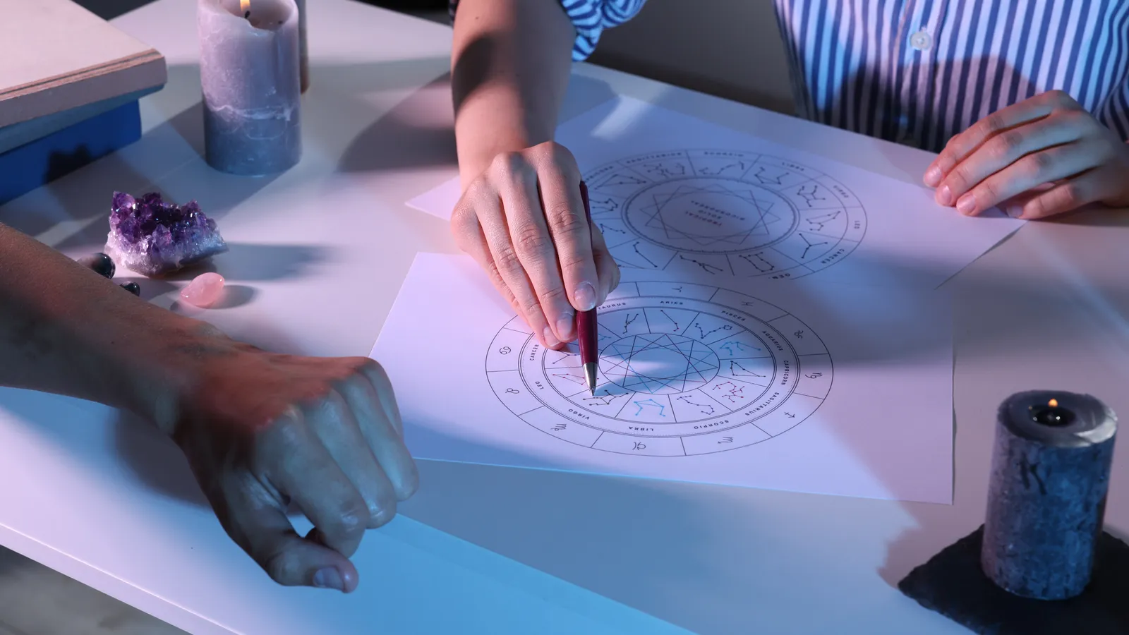 Astrologer's hands tracing a progressed chart over a natal wheel diagram